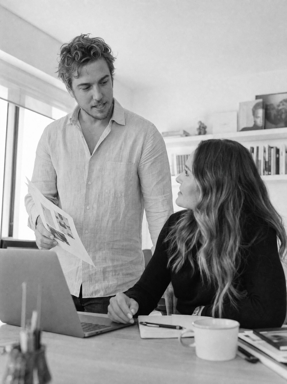 Robert showing Christianna a printed report while she works at a laptop, with hand-written notes marking where the time goes